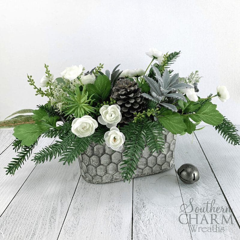 Rustic winter floral arrangement for table centerpiece. Metal honeycomb basket with pine, greenery, succulents, and white flowers. 