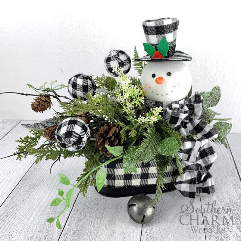 Winter table centerpiece with buffalo plaid snowman and ornaments and pinecones.