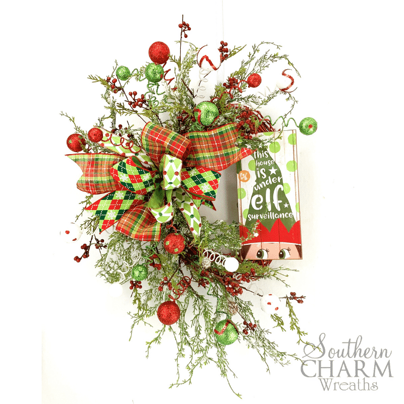 Red and green christmas wreath with ornaments, berries, and elf sign