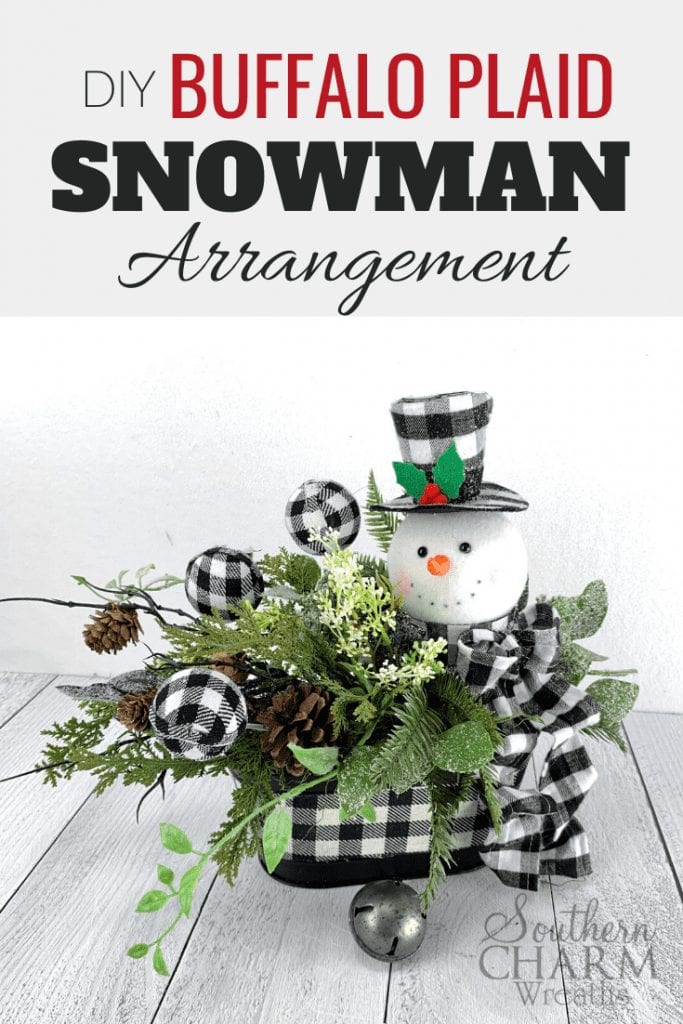 "DIY Buffalor Plaid Snowman Arrangement." Table centerpiece with buffalo plaid snowman and ornaments, with pinecones and greenery. 