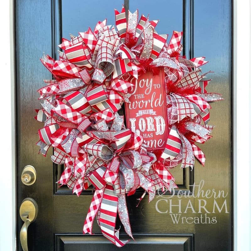 Joy to the world Christmas wreath using deco mesh and ribbon hanging on black front door. 