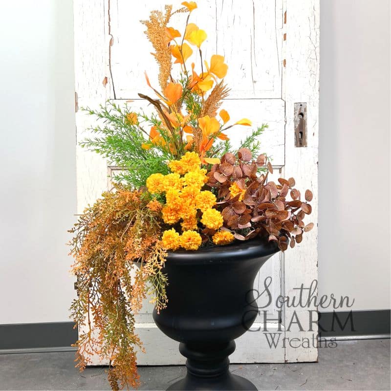 A black urn planter filled with fall flowers and foliage. 