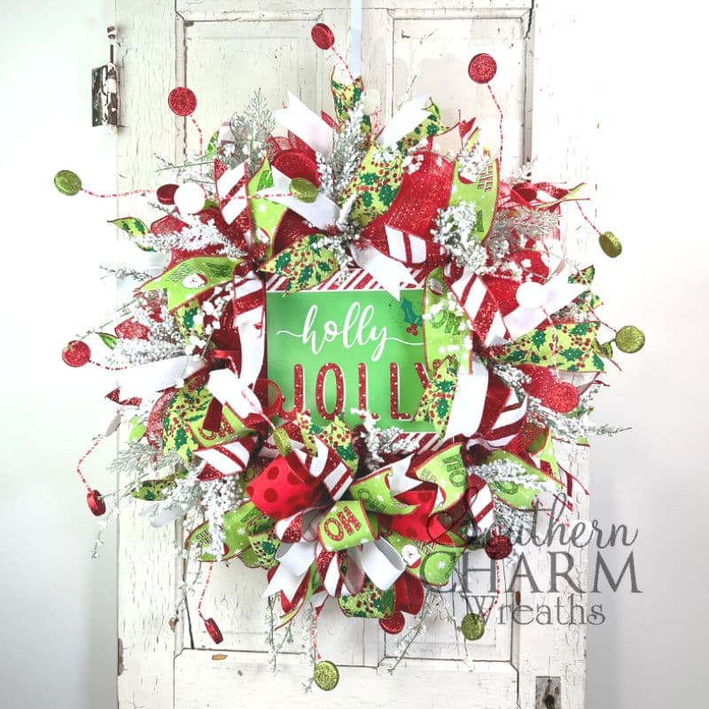 A deco mesh Christmas wreath with a green sign in the middle that reads "Holly Jolly" 