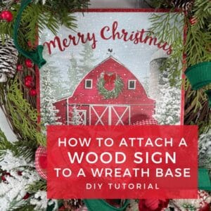 Christmas wreath decorated with greenery, berries, and plaid ribbon featuring a red barn wood sign that says Merry Christmas in the center.