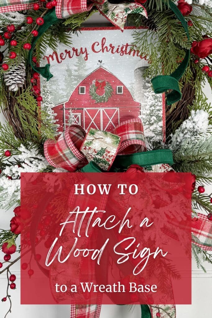 Christmas grapevine wreath with snowy greenery, red berries, plaid ribbon, and a red barn Merry Christmas wood sign. Text overlay reads How to Attach a Wood Sign to a Wreath Base.
