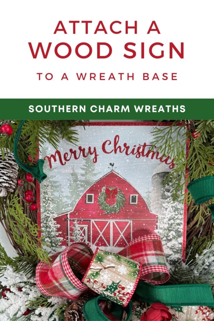 Close up of a Christmas wreath with greenery, berries, plaid ribbon, and a red barn Merry Christmas wood sign. Text overlay reads How to Attach a Wood Sign to a Wreath Base.