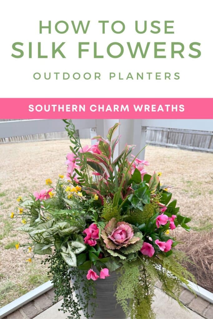 Overhead view of an outdoor planter filled with silk flowers — pink ornamental kale as the focal centerpiece, surrounded by pink geraniums and sweet pea-style filler blooms, yellow wildflower accents, variegated caladium foliage, and trailing greenery spilling over the pot edges. The arrangement sits in a gray ribbed pot on a covered porch. White header above reads: How to Use Silk Flowers Outdoor Planters in green text. Pink bar reads: Southern Charm Wreaths in white.