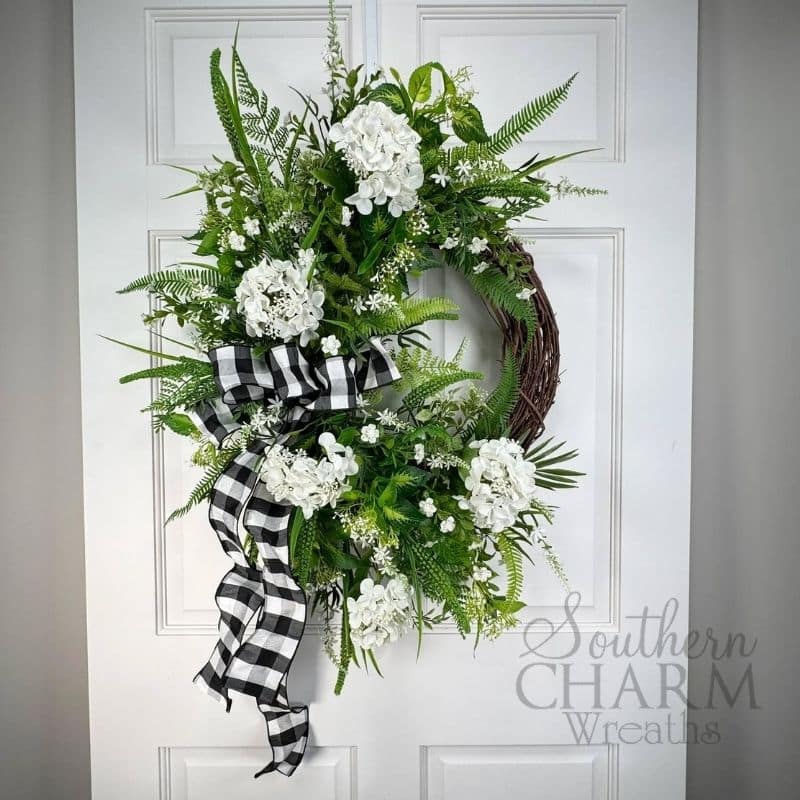 Grapevine wreath with greenery, hydrangeas, and checkered ribbon.
