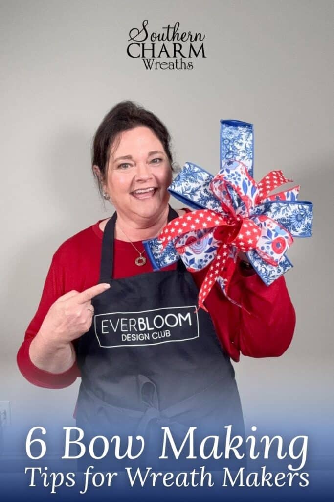 Julie Siomacco of Southern Charm Wreaths smiles and holds up a large patriotic multi-ribbon bow made from blue floral, red with white stars, and white with blue floral wired ribbons. She points to her black Everbloom Design Club apron. The Southern Charm Wreaths logo appears at the top. A blue gradient footer reads: 6 Bow Making Tips for Wreath Makers in white script.