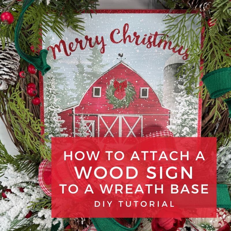 Christmas wreath decorated with greenery, berries, and plaid ribbon featuring a red barn wood sign that says Merry Christmas in the center.