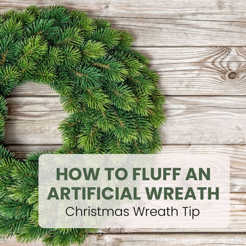 Fluffed artificial evergreen wreath with full pine branches on a wood plank background, text reads How to Fluff an Artificial Wreath